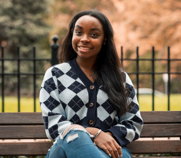 Marley DiTullio, smiling, sitting on a wooden slatted bench outdoors