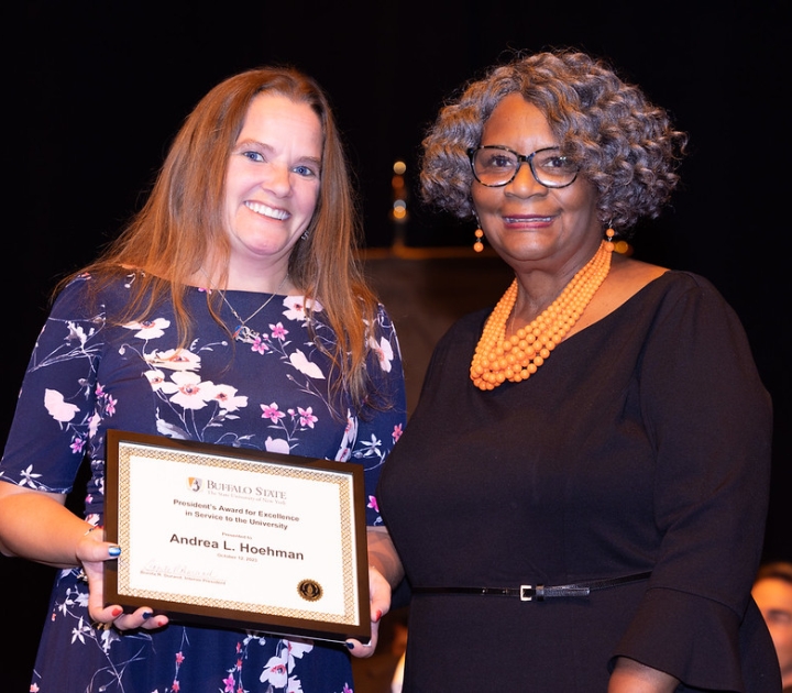 Andrea Hoehman displaying her framed award and standing with Interim President Durand